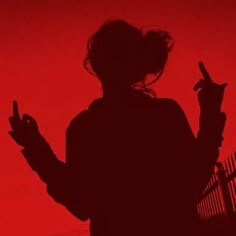 the silhouette of a woman holding a cell phone in her hand, against a red background