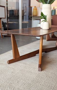 a wooden table sitting on top of a carpeted floor next to a vase filled with flowers