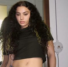 a woman with long curly hair standing in front of a mirror wearing a black top