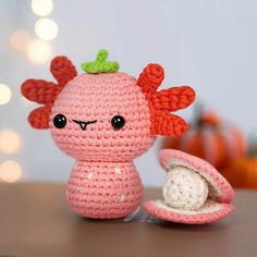 a pink crocheted doll sitting on top of a table next to an open shell