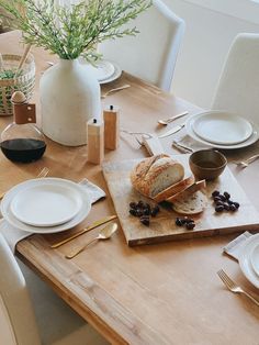 a wooden table topped with white plates and silverware