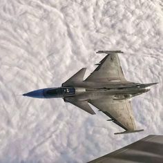 a fighter jet flying through the sky with clouds in the backgroud and below