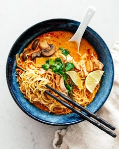 a blue bowl filled with noodles, mushrooms and lemons next to chopsticks