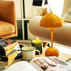 a stack of books sitting on top of a table next to a cup and lamp