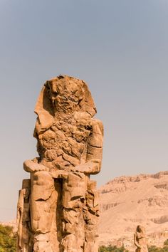 an ancient statue in the desert with mountains in the background