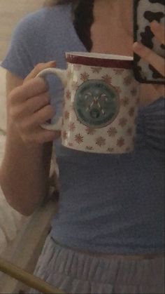 a woman taking a selfie with her cell phone and holding a coffee mug in her hand