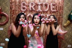 three women standing in front of a wall with balloons and confetti on it