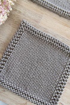 two knitted placemats sitting on top of a wooden table next to flowers