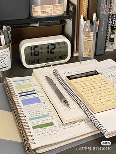 an open notebook sitting on top of a desk next to a clock and alarm clock