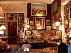 a living room filled with lots of furniture and bookshelves covered in pictures on the walls