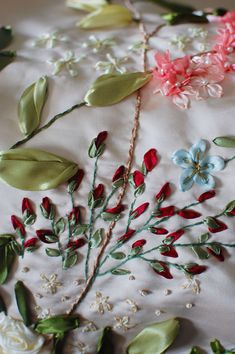 some flowers and leaves are laying on a white sheet with beads in the shape of branches