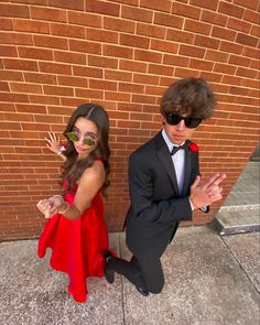 a young boy and girl dressed up in formal wear standing next to a brick wall