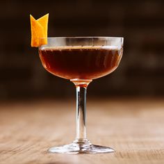 an orange peel sticking out of the rim of a glass filled with a dark colored drink