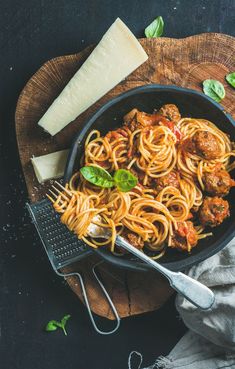 pasta with meatballs and sauce in a skillet on a wooden board next to cheese