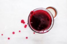 a glass filled with red liquid sitting on top of a white tablecloth next to a spoon