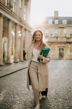 a woman is walking down the street with a book in her hand and smiling at the camera