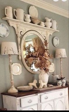 a white dresser sitting under a mirror next to a table with plates and cups on it