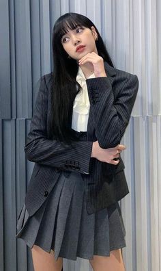 a woman in a skirt and jacket posing for the camera with her hand on her chin