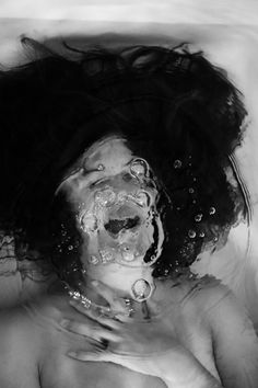 black and white photograph of a woman with her head submerged in water, taken from above