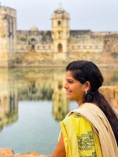 a woman standing in front of a body of water with a castle in the background