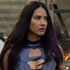 a woman with purple hair wearing a blue leather outfit and looking off to the side