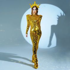 a woman in a gold bodysuit walking down the runway with a crown on her head