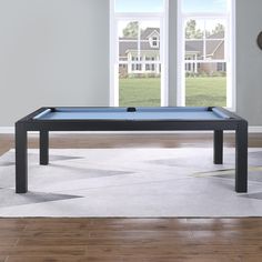 a pool table in the middle of a living room with large windows and wood floors