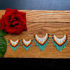 three pairs of beaded hoop earrings next to a red rose on a wooden surface