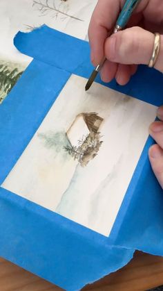 a person is drawing something on paper with a pencil and watercolors in front of them