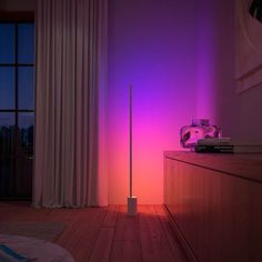 a pink and purple light shines on the wall next to a tall black pole