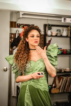 a woman in a green dress is holding her hand up to her face and looking at the camera