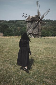 a woman in a long black dress walking towards a windmill