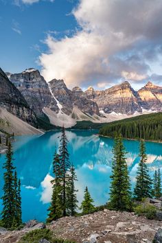 a lake surrounded by trees and mountains under a cloudy sky