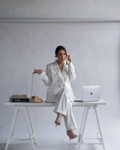 a woman sitting at a desk with a laptop and phone in her hand, holding a string