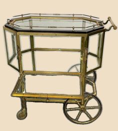 a glass and metal cart with wheels on the front, sitting against a beige background