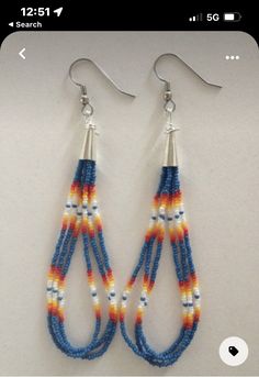 two pairs of beaded earrings are hanging from hooks on a white surface, one is blue and the other is orange