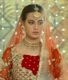 a woman in a red and gold bridal gown with jewelry on her head, wearing an orange lehenga