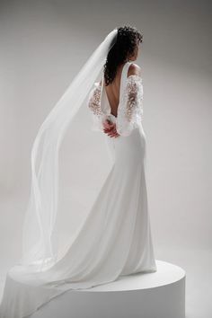 a woman in a white wedding dress with a veil on her head is looking back