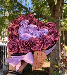 a person holding a large bouquet of purple and pink roses in front of a tree