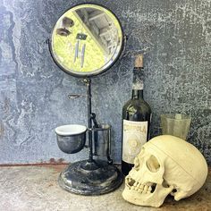 a bottle of wine sitting next to a skull and a mirror on a table with a bowl