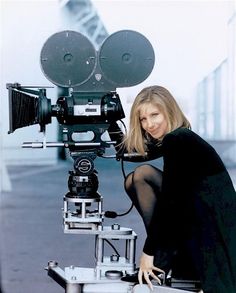 a woman kneeling down in front of a camera on top of a tripod next to a building