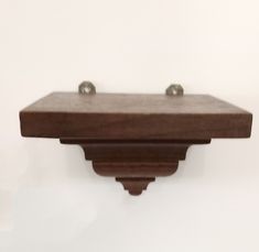 a wooden shelf with two metal knobs on it's sides and a white wall in the background