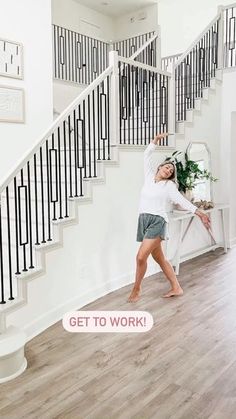 a woman standing in front of a stair case next to a white wall and wooden floor