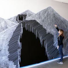 a woman is standing in front of a large piece of art that looks like mountains