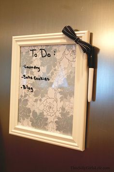 a white frame hanging on the wall with a black ribbon attached to it that says to do