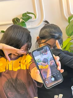 two people sitting at a table with one holding up a cell phone in front of the other