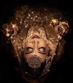 a woman with makeup on her face and head covered in gold sequins is looking up at the camera