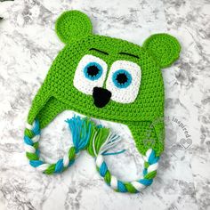 a green crocheted hat with eyes and ears on top of a marble surface