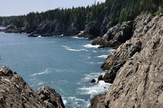 the ocean is surrounded by rocky cliffs and pine trees