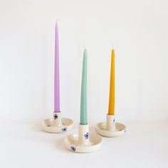 three candles are sitting in small dishes on a white surface, one is yellow and the other two are blue